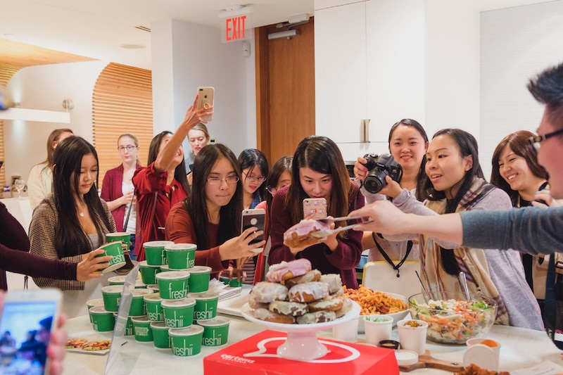 Mujeres jóvenes en un evento social comiendo y tomando fotos de la comida.