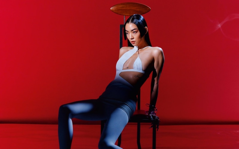 La cantante japonesa del pop Rina Sawayama, reclinada sobre una silla sobre un fondo color rojo