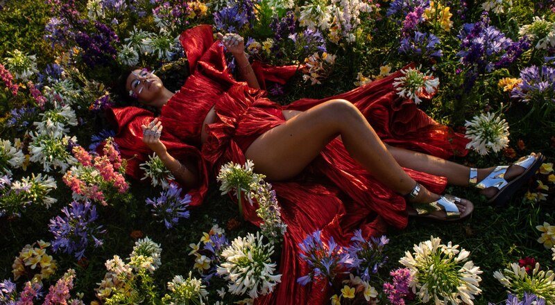 Mujer en vestido rojo acostada en un campo de flores