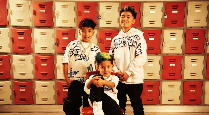 Tres niños sonríen frente a una pared de casilleros escolares.