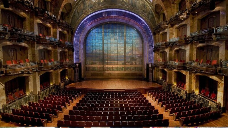 Un teatro vacío con butacas rojas y un escenario iluminado