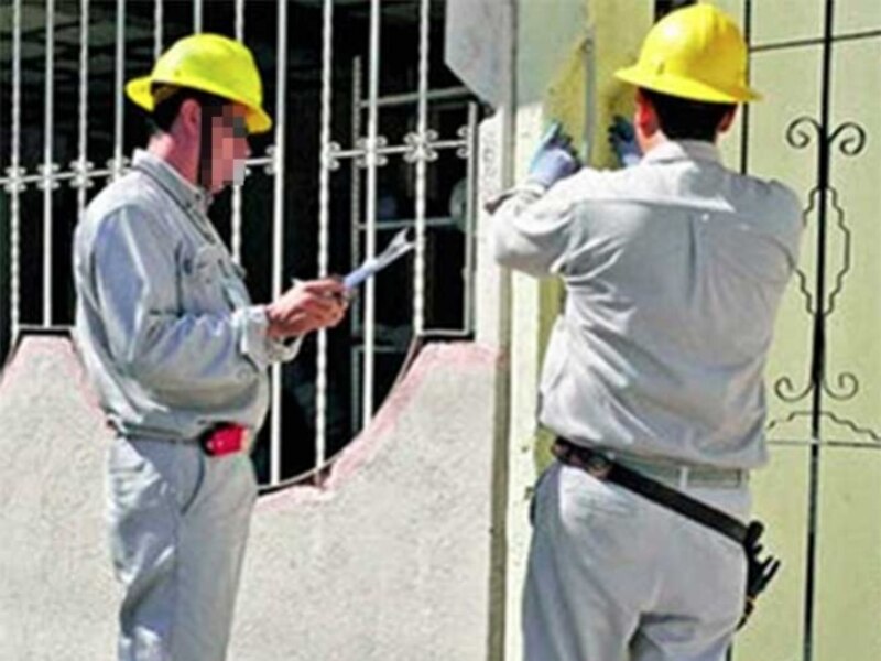 Dos hombres vestidos con uniforme y casco de seguridad están trabajando en una fachada de una casa