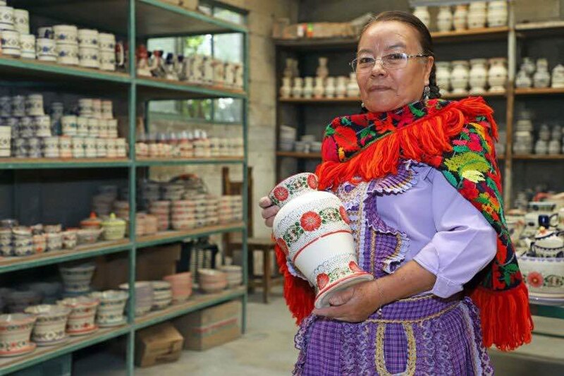 Artesana mexicana sostiene un jarrón de cerámica pintado a mano