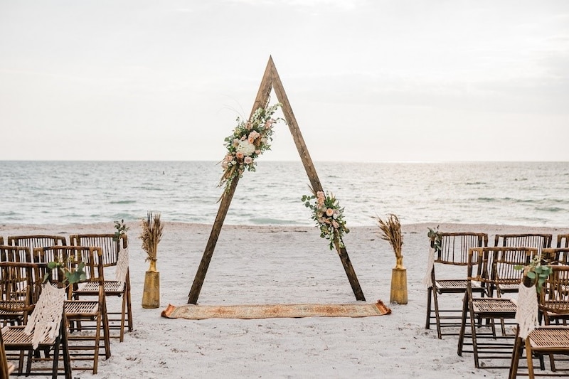 Boda en la playa con arco de madera y sillas de mimbre