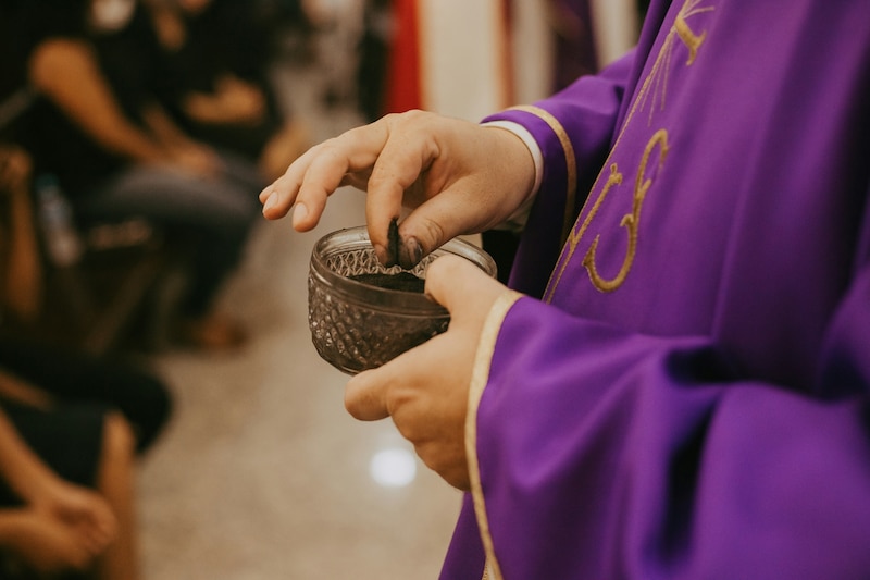 Imagen de un sacerdote colocando ceniza en sus manos previo a marcar la frente de las y los creyentes con una cruz en el miércoles de ceniza.