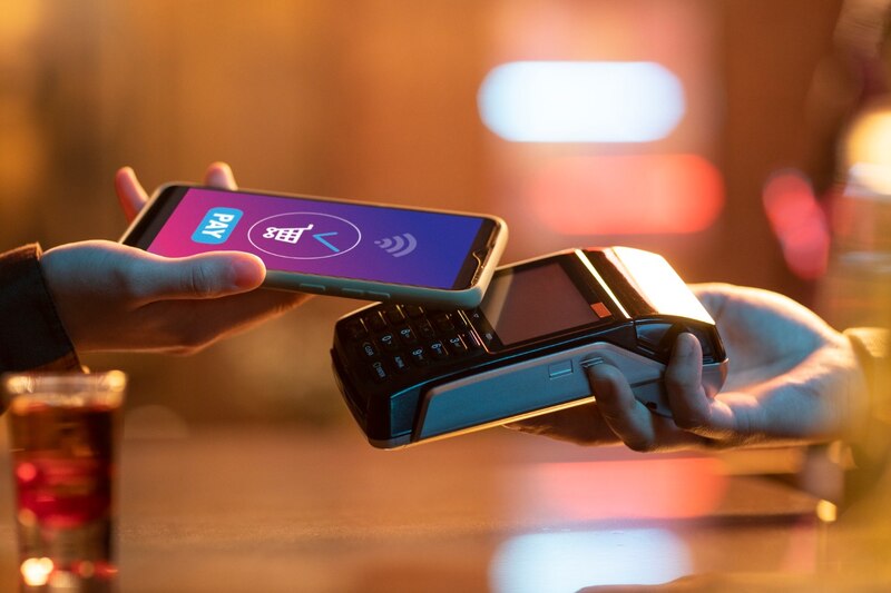 Mano acercando un celular a un lector de pagos para hacer una transacción sin contacto