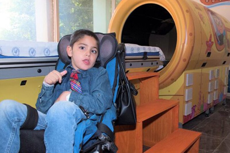 Niño en silla de ruedas junto a una cama de hospital decorada con motivos marinos.