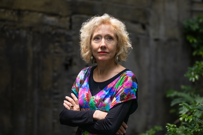 Retrato de una mujer de mediana edad con el pelo corto y rubio, que lleva una camisa estampada de colores vivos.