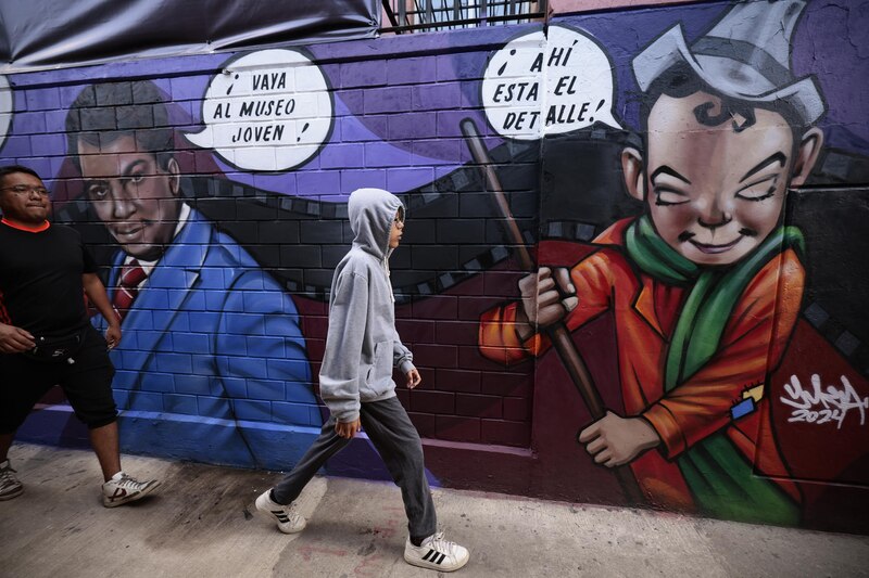 Un joven camina frente a un mural de Cantinflas