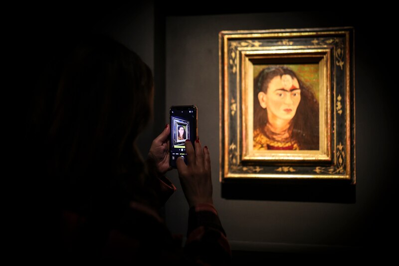 Mujer tomando una foto de la pintura de Frida Kahlo "Autorretrato con mono".