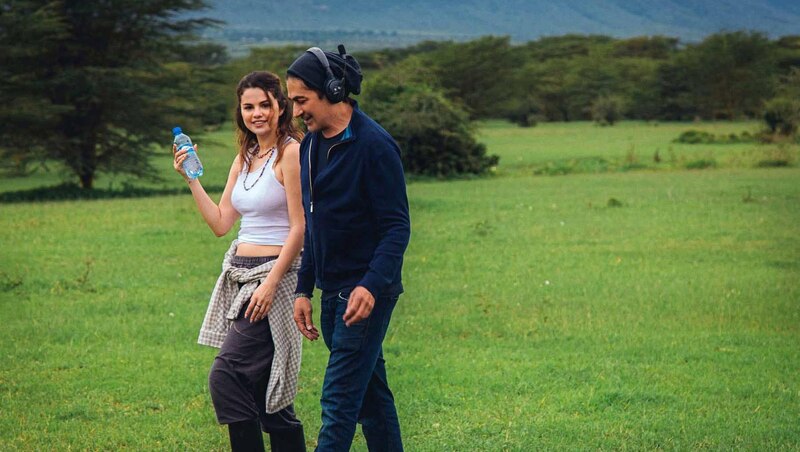 Selena Gomez y el director de cine Steven Spielberg caminan por un campo verde en África.