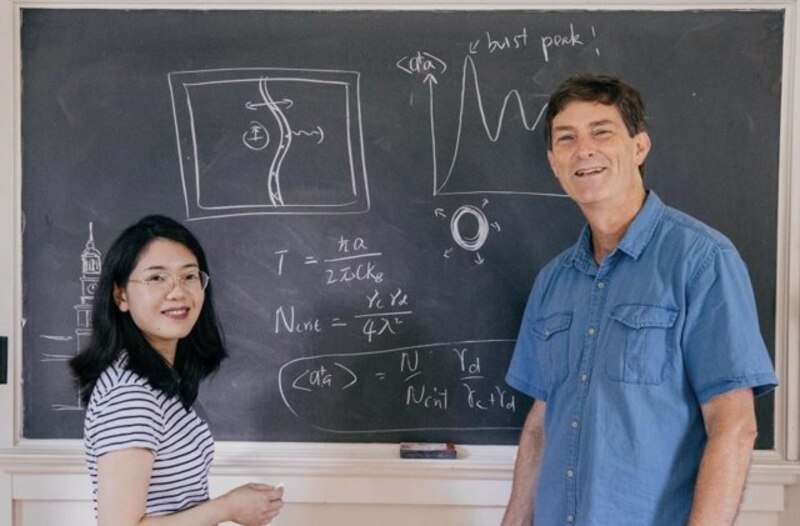 Profesora y estudiante de pie junto a una pizarra.
