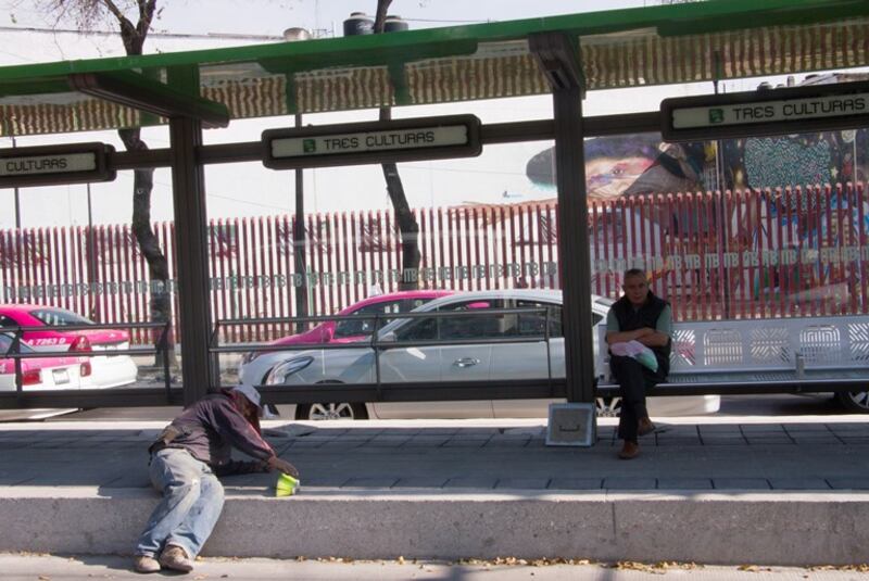 Un hombre barre la calle mientras otro espera el autobús