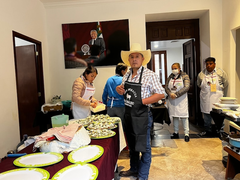 Un hombre con sombrero de vaquero observa cómo dos mujeres preparan comida en una mesa.