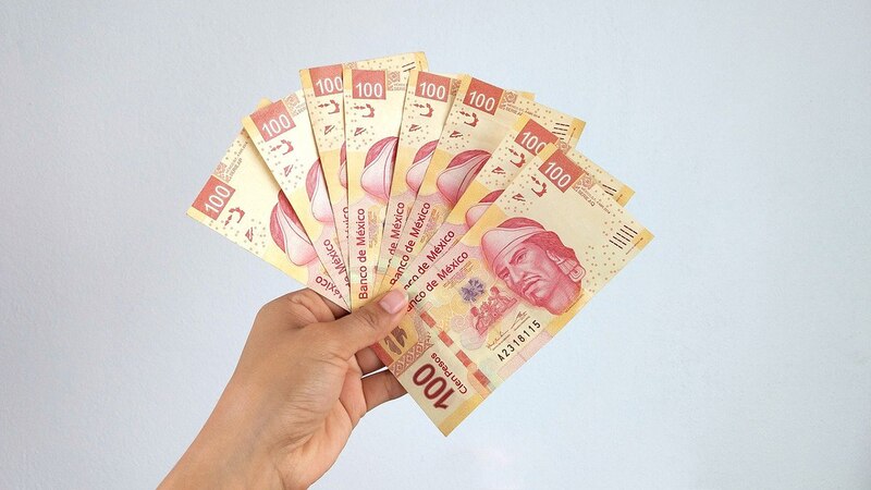 Un fajo de billetes de 100 pesos mexicanos en la mano
