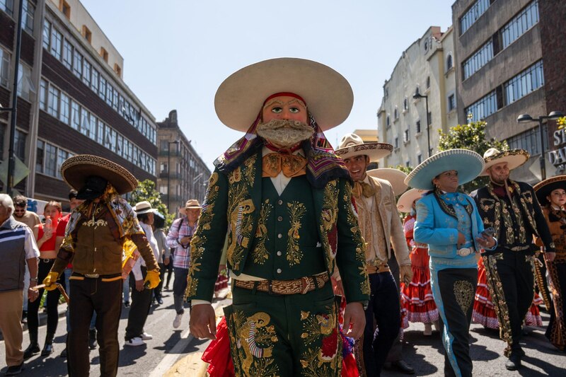 Un hombre con un traje verde y un sombrero negro baila en una calle de la Ciudad de México.