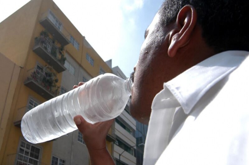 Un hombre bebe agua de una botella en la calle