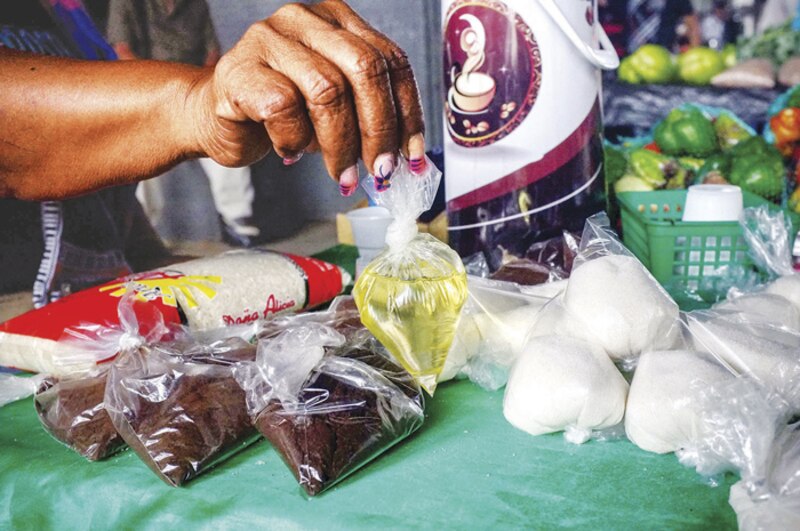 La imagen muestra a una persona comprando productos alimenticios en un mercado local.