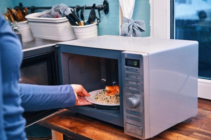 Persona introduciendo un plato con alimentos en un horno de microondas