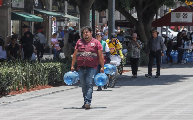 Un hombre camina por la calle cargando dos garrafones de agua
