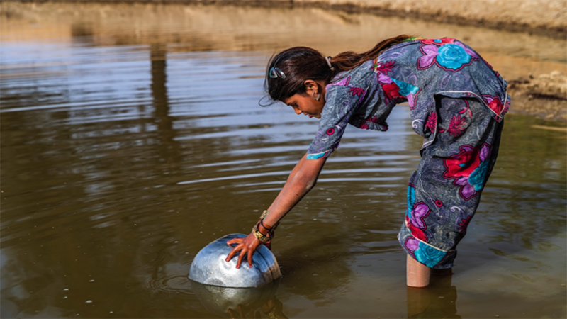 Niña recogiendo agua de un río