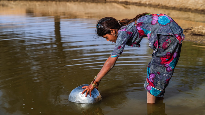 Niña recogiendo agua de un río