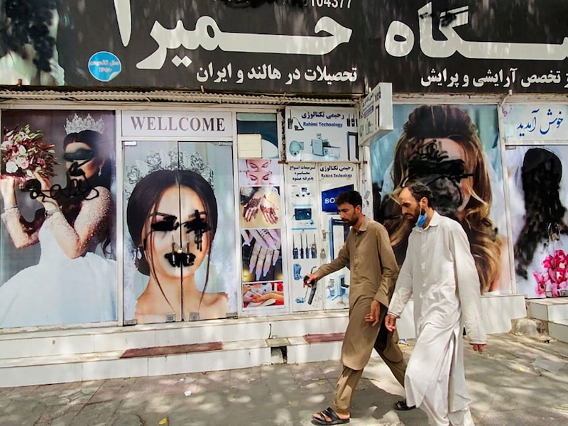 Dos hombres caminan frente a un salón de belleza en Kabul, Afganistán.