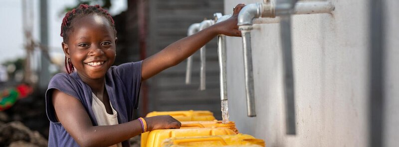 Niña africana sonriendo mientras llena una jarra de agua limpia