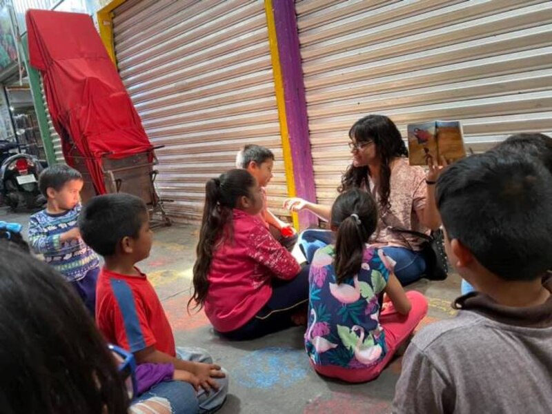 Voluntaria lee un libro a un grupo de niños en un mercado