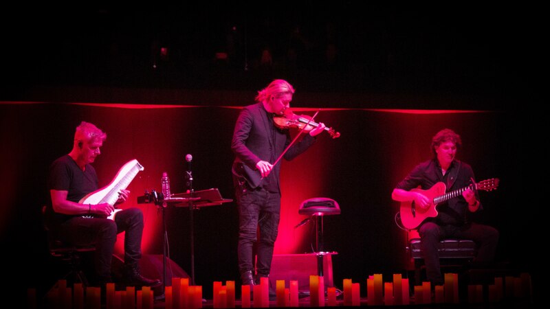 Trío de músicos tocando en un escenario con velas.