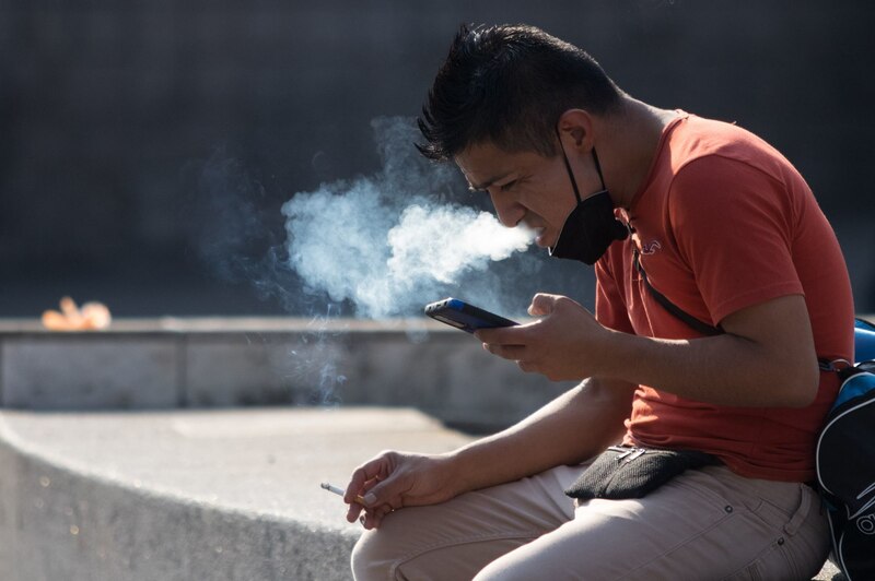 Joven fumando y mirando su teléfono