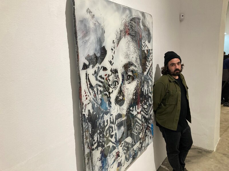 Artista urbano posando junto a su obra.