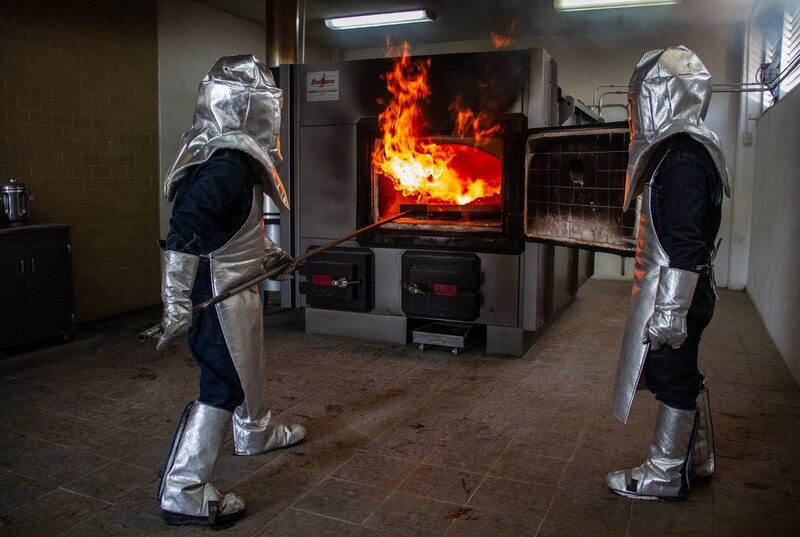 Dos hombres con trajes protectores y máscaras trabajan en un horno crematorio