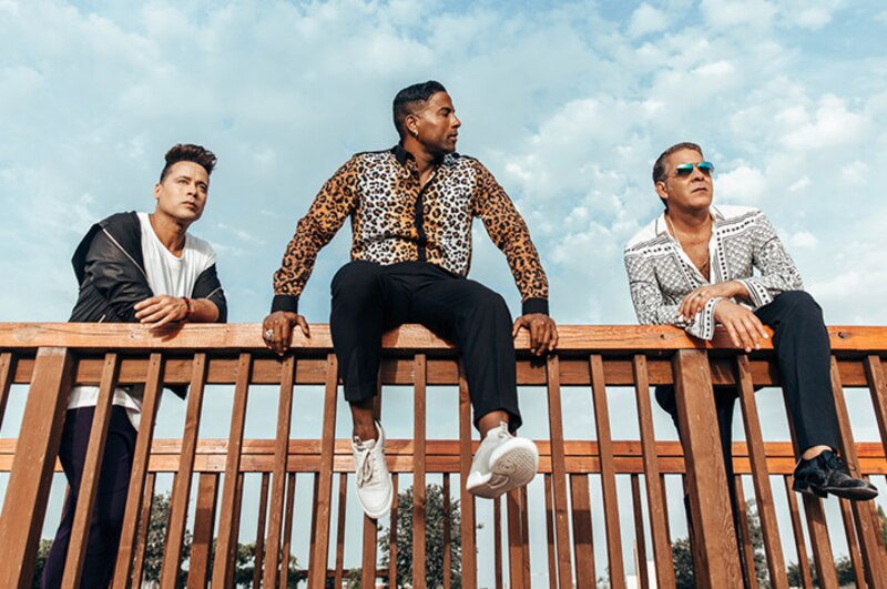 Tres hombres latinos vestidos con ropa casual en un balcón