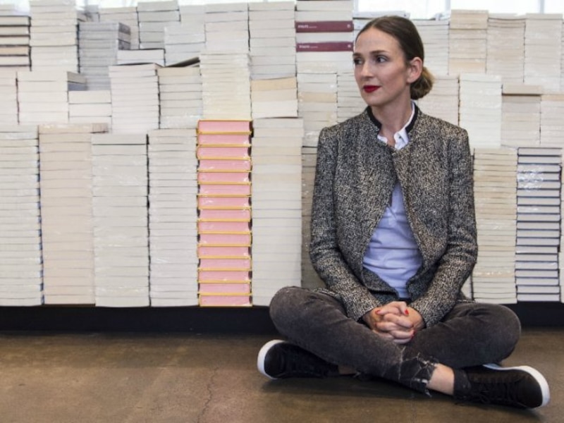 La escritora española María Dueñas, sentada frente a una montaña de libros.