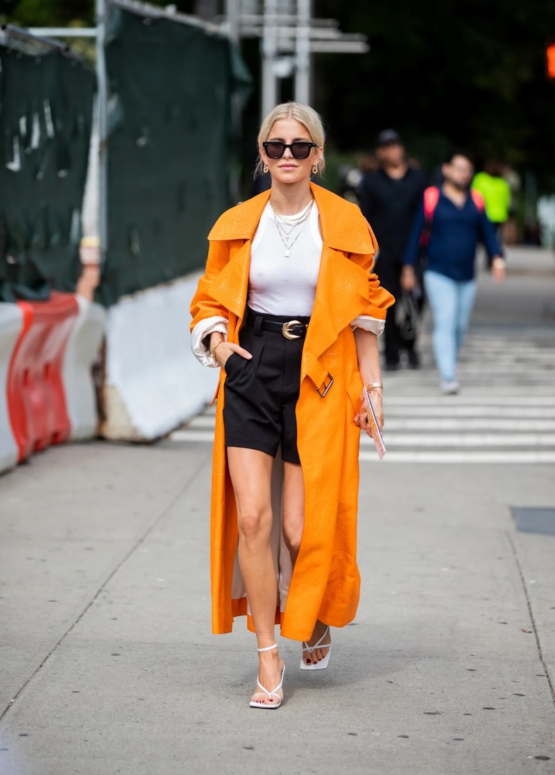 Modelo vistiendo una blusa blanca, shorts negros y un abrigo naranja