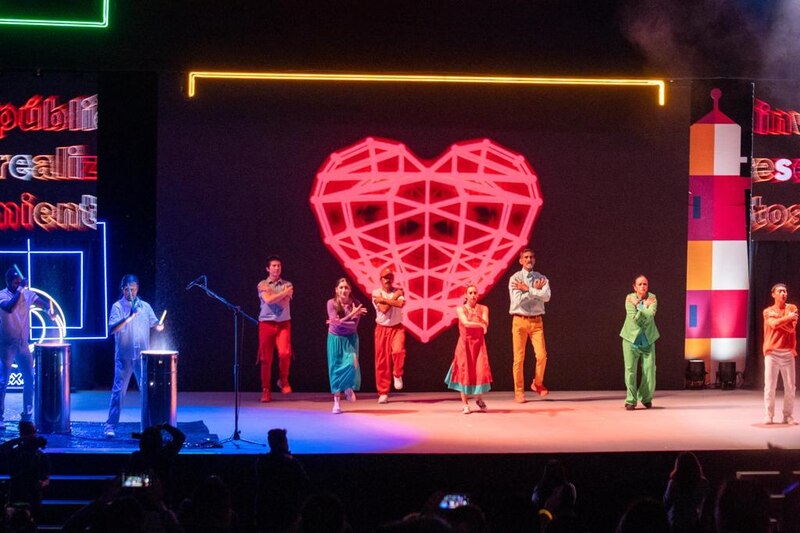 Una imagen de un grupo de personas bailando en un escenario con un corazón rojo de fondo.