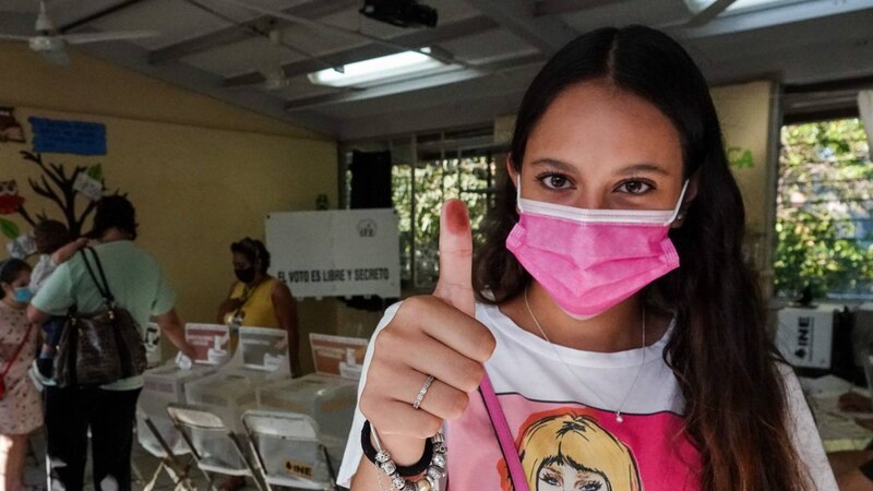 Mujer joven con mascarilla en una cabina de votación