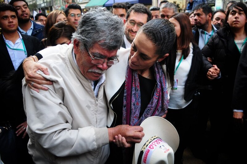 AMLO y Sheinbaum se abrazan en un evento público.