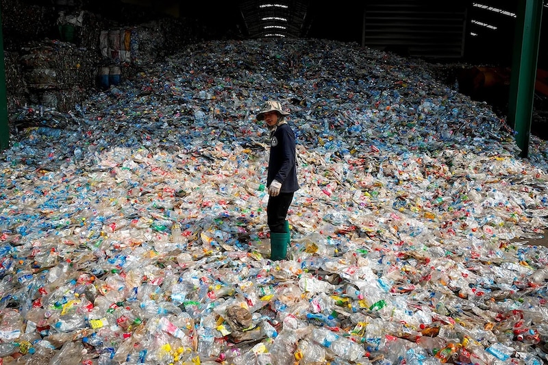 Un hombre se encuentra en medio de una montaña de botellas de plástico.