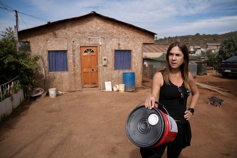 Mujer sosteniendo un balde rojo frente a una casa de madera