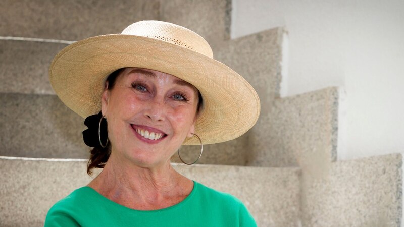 Elegante mujer mayor con sombrero de paja y blusa verde sonríe a la cámara