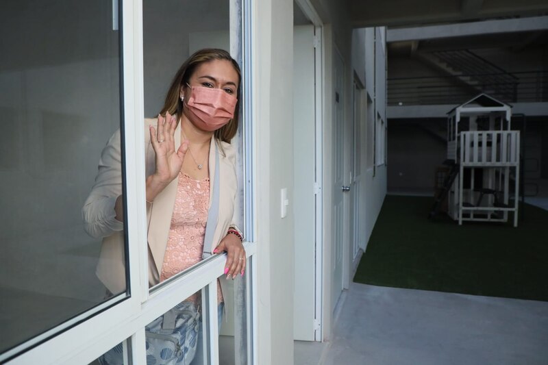 Mujer joven saluda desde la ventana de su casa