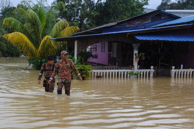 Autoridades y Oficiales del Departamento de Bomberos y Rescate de Malasia inspeccionan viviendas afectadas por las inundaciones en Klang