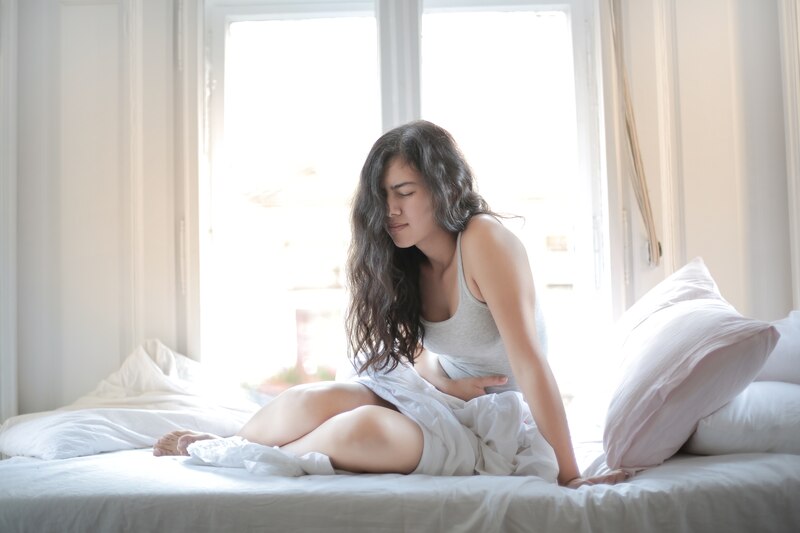 Mujer joven sentada en la cama con dolor de estómago