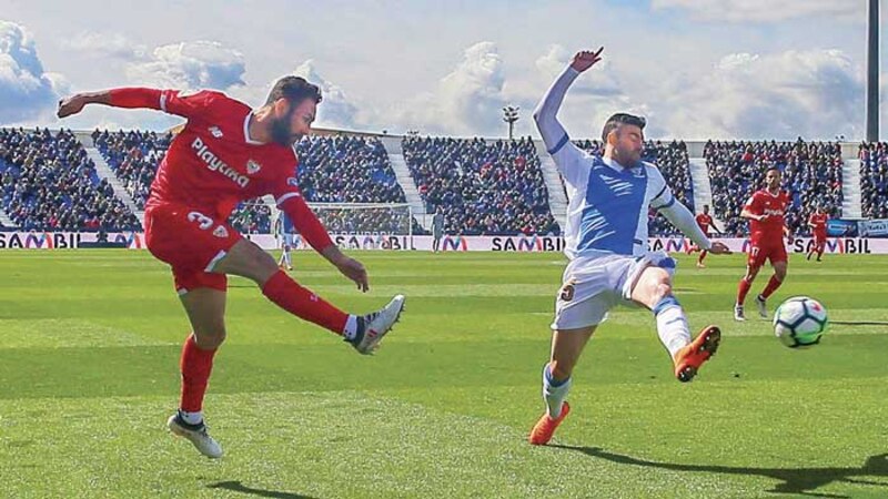 Dos jugadores de fútbol disputan un balón en el aire.