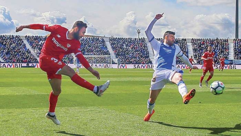 Dos jugadores de fútbol disputan un balón en el aire.