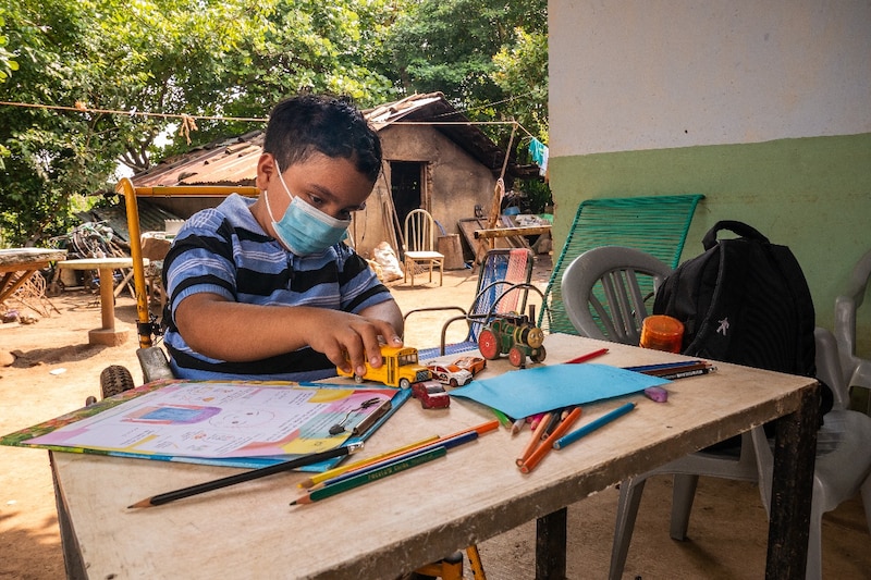 Niño con discapacidad física en silla de ruedas jugando con carritos de juguete y lápices de colores