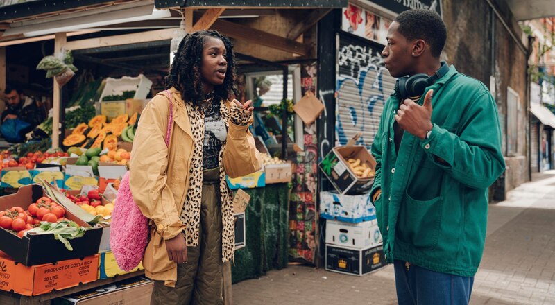 Dos jóvenes conversan en un mercado de frutas y verduras.