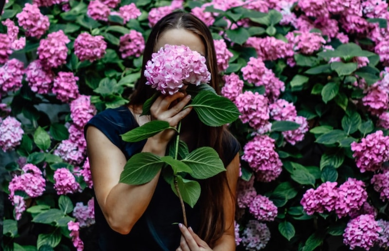 Mujer sosteniendo un ramo de flores sobre un muro de flores